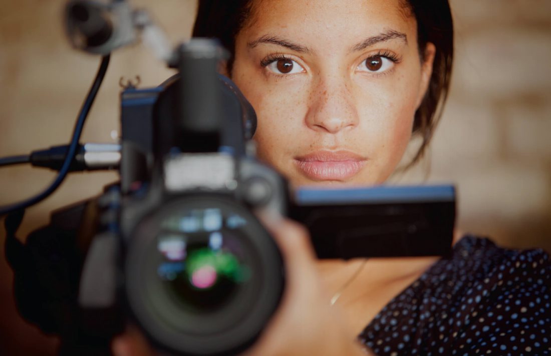Woman looking at camera, holding video camera pointed at the viewer