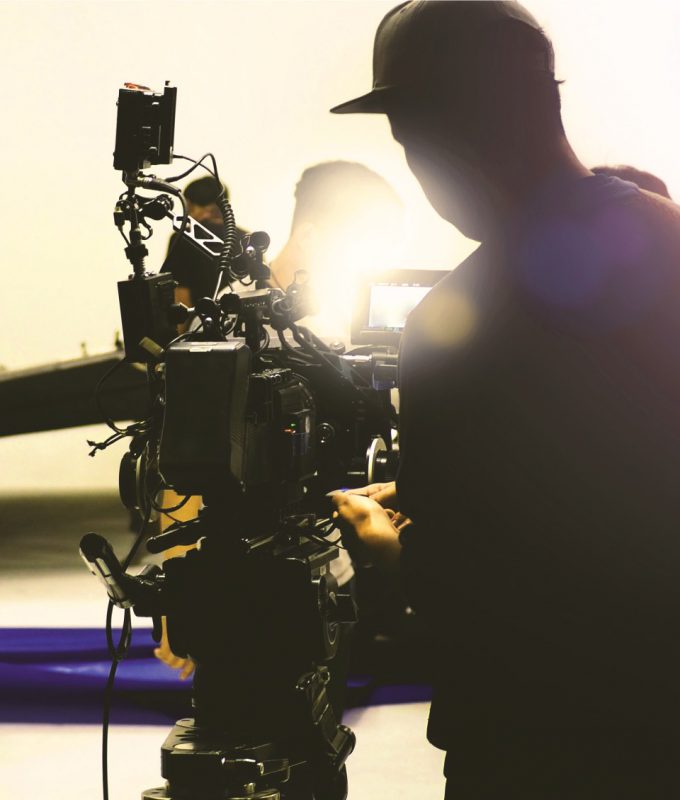 Photo of a cameraman. Taken from behind. Cameraman silhouetted with lens flare from studio lighting.